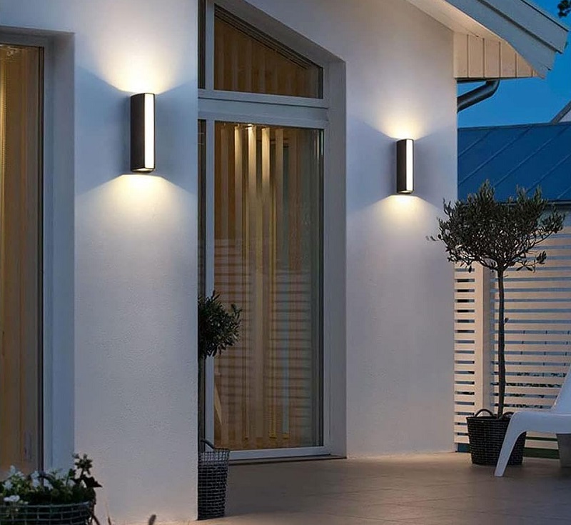 Modern vertical LED wall lights create light and shadow effects on the front wall of a house.