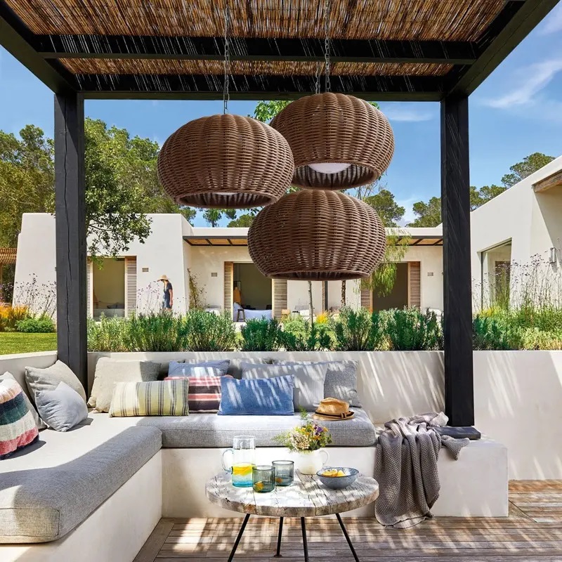 Bohemian-style rattan pendant lamp hanging above a dining table in an outdoor pergola.